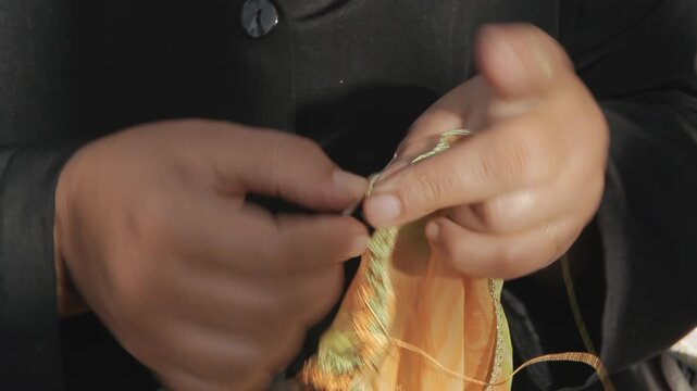 Close-up of hands using a hook to crochet a traditional lace border on an orange fabric. Handmade craft, sewing, needlework and cultural heritage concept.