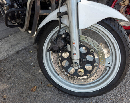 TAVERNES BLANQUES, SPAIN - JUNE 14, 2026.Detailed view of the front wheel, brake disc, caliper, and fork of a vintage white Suzuki motorcycle during a sunny day