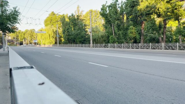 A wide empty road stretches through Simferopol, Crimea. Lush green trees line the quiet street. This serene scene brings a deeply peaceful and lonely feeling to a bright summer morning.