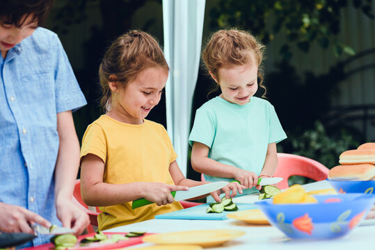 Children learning safe knife skills while preparing fresh vegetables outdoors