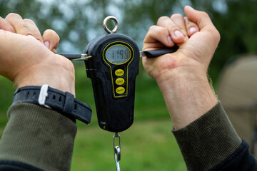 Digital fishing scale held by angler outdoors during carp fishing © Mati