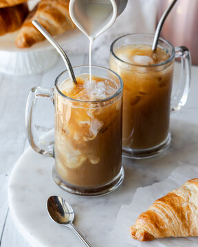 A marble slab topped with glasses of iced coffee with milk being poured into one