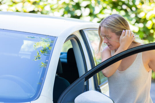 Young Caucasian woman with blonde hair getting into a white car, tucking her hair behind her ear with a gentle smile