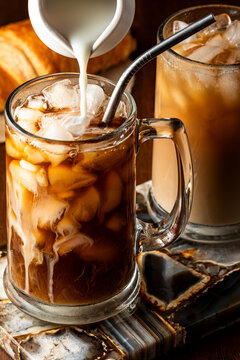 Pouring milk into a glass of iced coffee with a mixed one in behind.