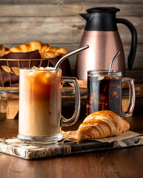 Glasses of iced coffee served with croissants against a dark background.
