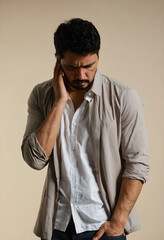 Fototapeta premium Young adult man with a pained expression holding his ear, suffering from headache or earache, isolated on a beige background