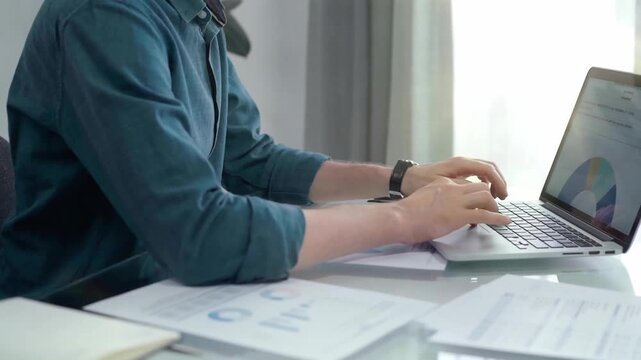 Professional working at laptop with data analysis charts. Businessman analyzing statistical data on a laptop next to business reports. Business concept