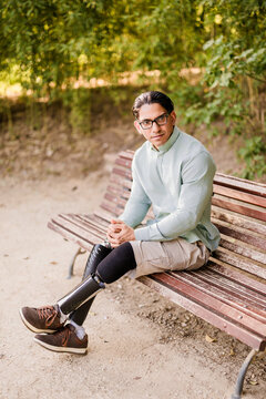 Latino man with prosthetic legs sitting on park bench