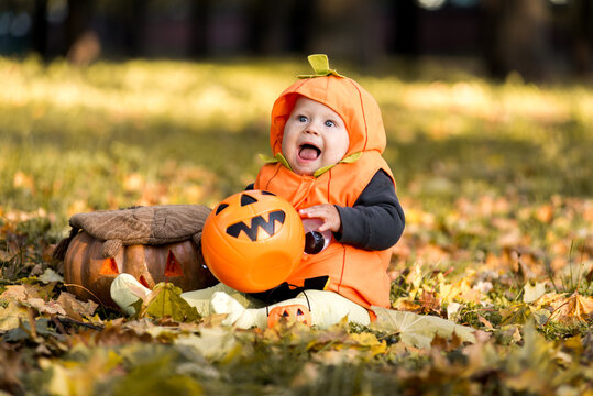 Cute baby in pumpkin costume sitting in autumn leaves with jack-o-lantern