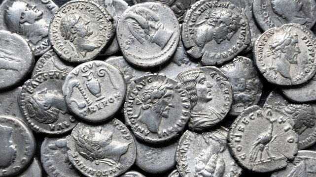 Close-up of ancient Roman silver coins in a money pile. Macro photography of old metallic currency with emperor profiles. History, antique and archaeology background