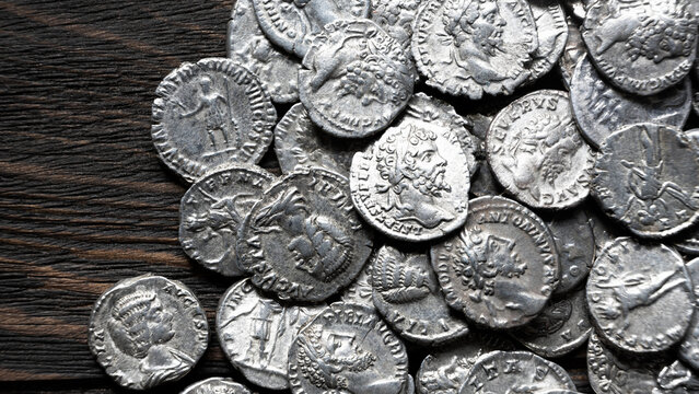 Pile of ancient Roman silver coins on a dark wooden background. Collection of silver denarii featuring portraits of emperors. Historical numismatics and archaeology concept.