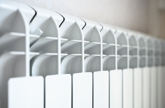 Close-up of a modern white central heating radiator. Detailed view of metallic fins on a home wall heater. Indoor temperature control and energy concept