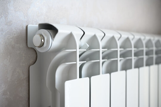 Close-up perspective of a modern white radiator and valve. Central heating system detail in a home interior. Domestic plumbing and temperature control