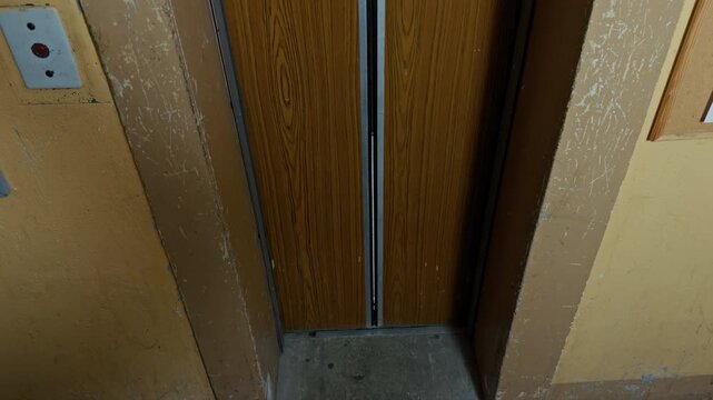 Worn elevator doorway with sliding wooden doors and scratched interior walls inside old building
