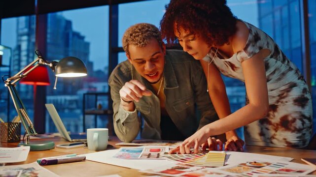 Designers discussing color swatches evening office, colleagues brainstorming