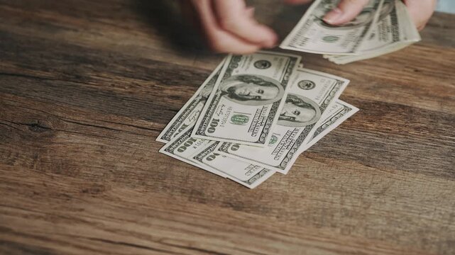 Person sorts and counts US dollar bills on a rustic wooden surface. Visual representation of budgeting, household expenses, financial management, cash savings, income, and everyday economic activity.