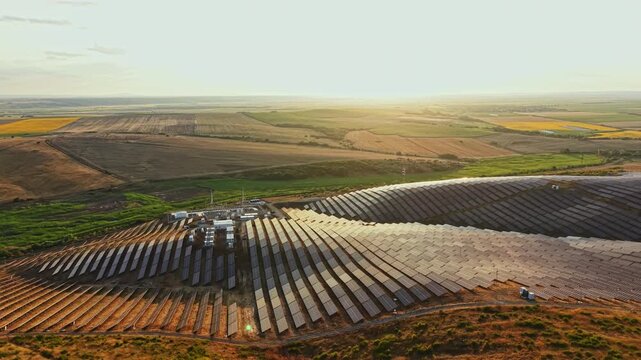 Rows of solar panels sit on a farm in a wide open area as the sun sets behind distant fields. The scene shows a commitment to clean energy.