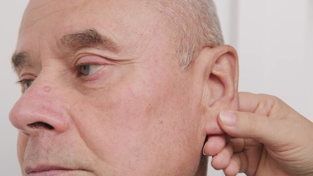 bald man hearing or listening deeply, ear with pained expression, discomfort loud noise, age-related hearing loss, Emotional portrait, discomfort loud noise, Environmental noise, reaction loud sounds