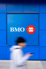 Fototapeta premium Toronto, Canada - June 19, 2026: Blurred pedestrian walking past BMO bank logo on blue wall