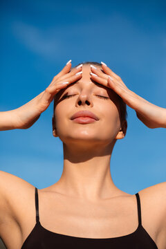 Attractive woman covering forehead from bright summer sunshine. Beauty woman displaying radiant complexion with healthy skin. Sun care concept.