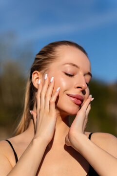 Portrait of female model touching soft glowing facial skin. Beautiful woman enjoying healthy complexion with natural skincare. Beauty wellness concept.
