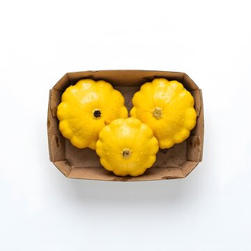 Three yellow pattypan squash in a cardboard box on white background