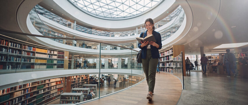 Student reading book in modern library while walking on a circular wooden walkway with glass railings under bright atrium light, suitable for university education and study visuals