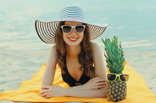 Summer vacation, happy smiling young woman with pineapple in hat with sunglasses lying on sea beach