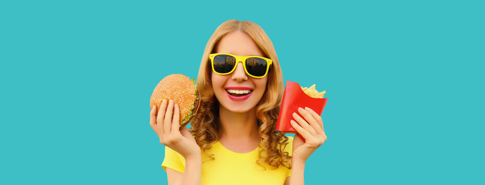Portrait of happy cheerful young woman eating burger fast food and french fries