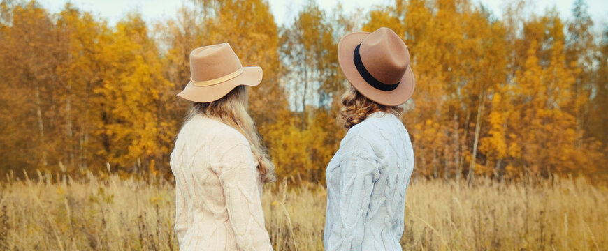 Two women friends together in autumn park, stylish girlfriends in hat, trees with yellow leaves