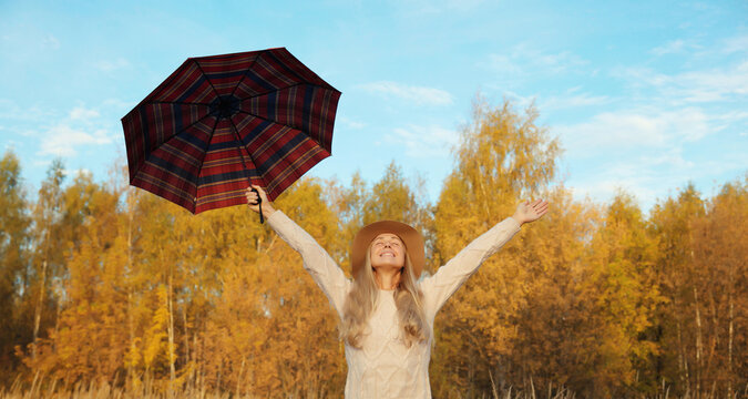 Happy woman in autumn park with umbrella, enjoying warm weather, trees with yellow leaves
