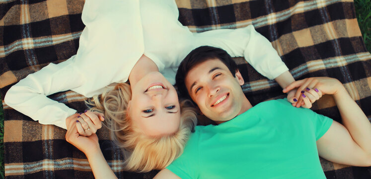 Portrait of beautiful happy smiling young couple in love lying together on a blanket, summer park