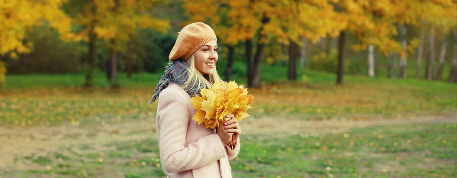 Beautiful happy smiling young woman holding yellow maple leaves with french beret in autumn park