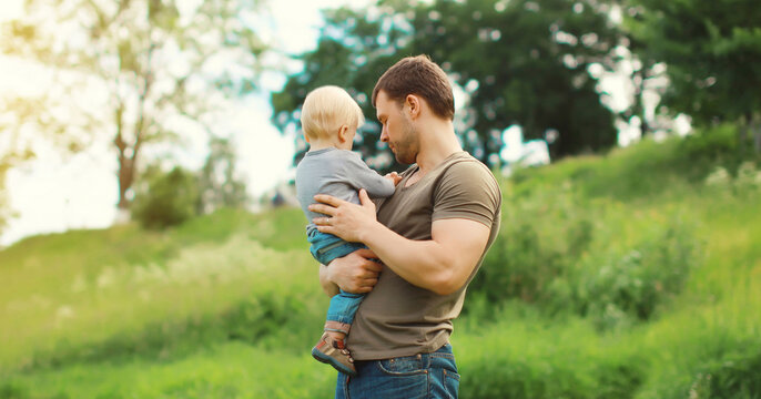 Caucasian father holding his son, dad and child walking together in summer park