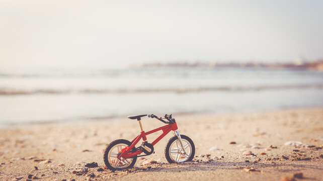 Miniature red bicycle on sand of sea beach as a concept of green travel and eco tourism