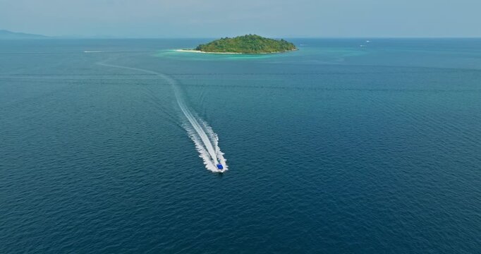 Speedboat quickly moving across calm turquoise sea, leaving long white wake trail, small lush green islands, and open ocean, creating a paradise tropical vacation landscape. Phi Phi Islands boat tour