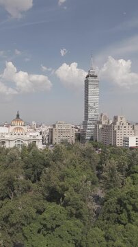 Aerial reveal shot ascending above Alameda Central treetops to unveil Torre Latinoamericana and historic center, vertical video, Mexico City, shot in D-Log M