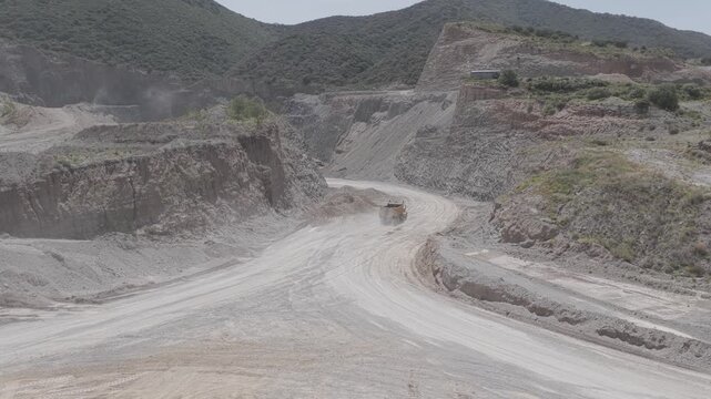 Loaded mining truck climbing dusty uphill road through open-pit quarry, shot in D-Log M