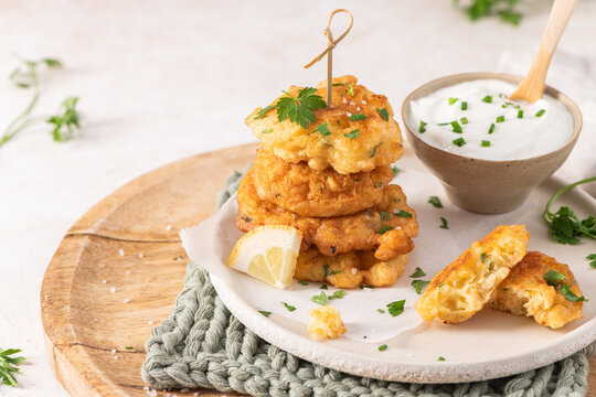 Crispy golden cod fish fritters stacked on a rustic plate with creamy dipping sauce fresh herbs and a lemon wedge for a perfect appetizer snack