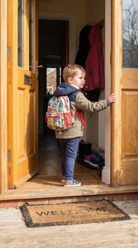 A young boy with a backpack stands in an open doorway looking outside. It captures the spirit of adventure and the beginning of a new experience. Ideal for travel blogs and parenting articles.