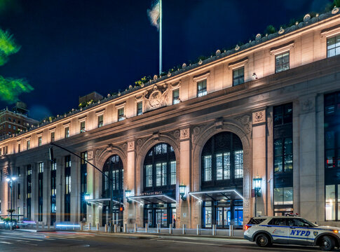 New York, NY - US - Jul 20, 2026 Night view of Moynihan Train Hall in New York City, its grand Beaux-Arts facade illuminated, traffic streaks and an NYPD vehicle adding urban motion and atmosphere!
