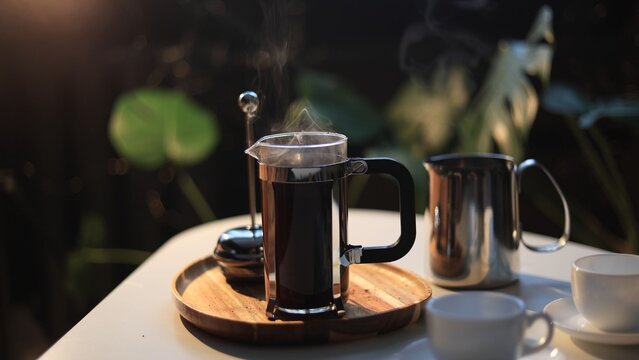 Steaming French press coffee on a wooden tray with cups and milk pitcher