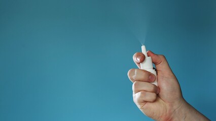 Obraz premium Hand holding a white nasal spray bottle and spraying mist against a blue background
