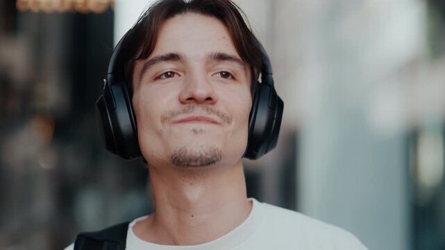 Young man listening to music with black over-ear headphones outdoors