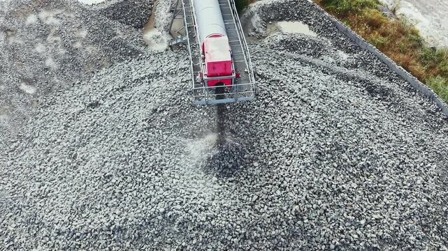 In a granite quarry, a machine works to crush large stones into smaller pieces. The scene shows the machinery processing granite at a mining site during daylight hours.