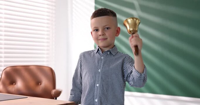 Cute boy ringing school bell in classroom