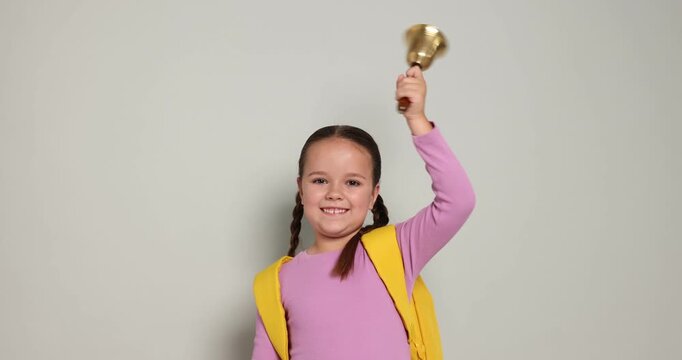 Cute girl ringing school bell on light grey background