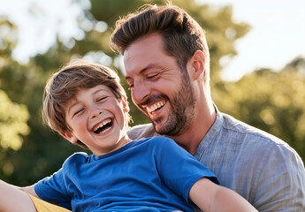 Fototapeta premium Close-up of a smiling father and laughing son sharing a joyful outdoor moment in warm summer sunlight with blurred green park background.