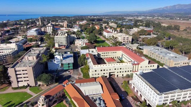 Aerial motion over university of california santa barbara campus buildings on sunny day with ocean backdrop.