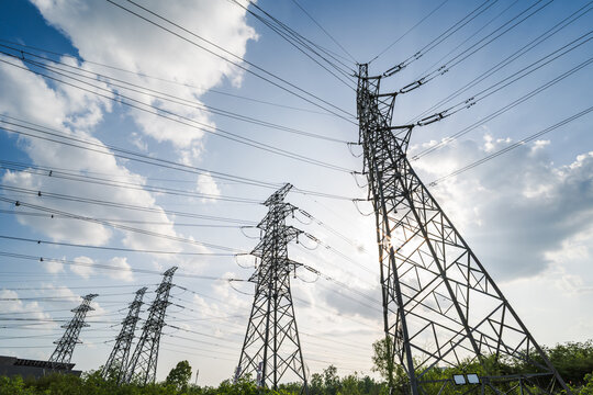 Multiple high-voltage transmission towers stand under a blue sky with white clouds, supporting power lines.